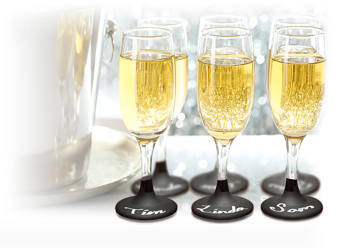 Fyra champagneglas med gult innehåll på ett bord, med svarta markörer med namn under varje glas