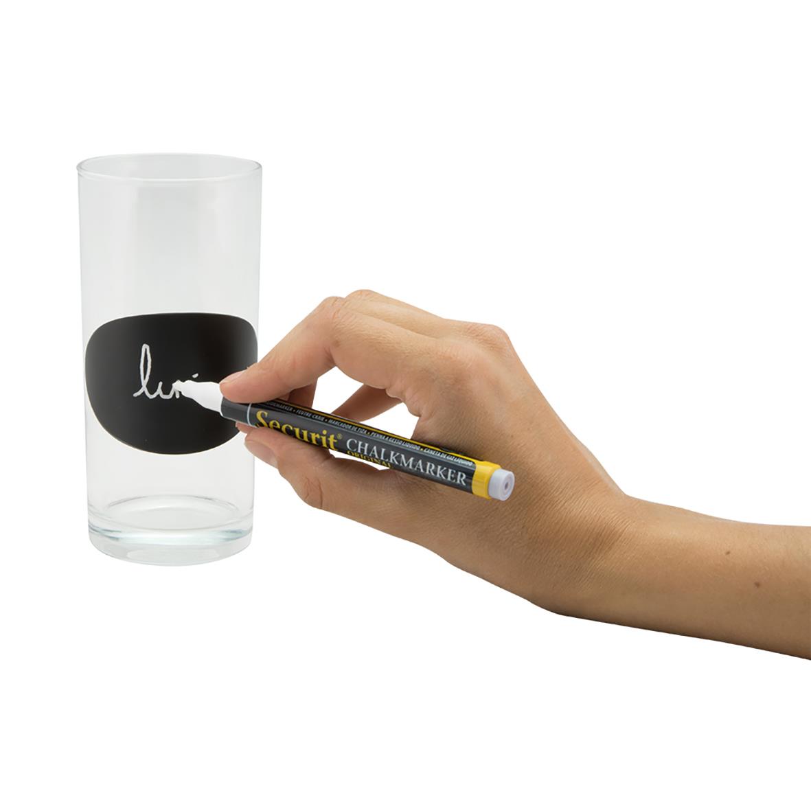 Person skriver på ett svart griffelklistermärke Securit Oval på ett glas med en vit penna