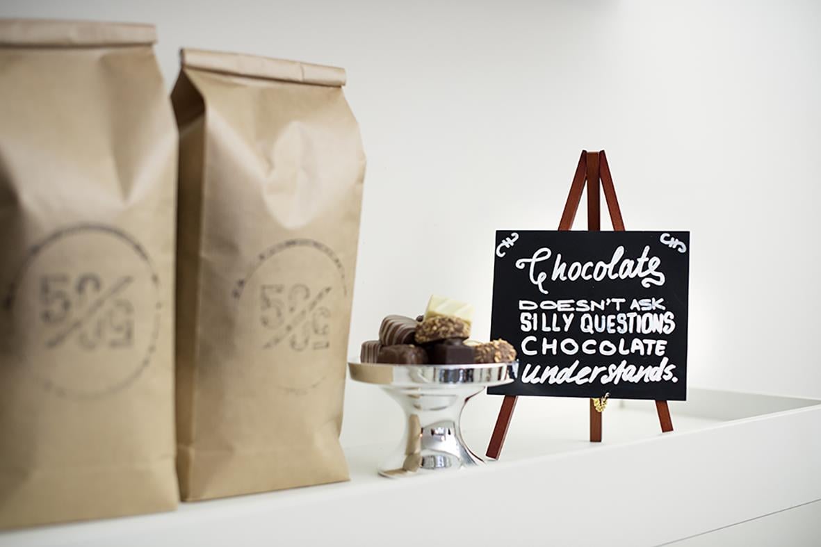 Svart griffeltavla med vitt skrivande, omgiven av bruna papperspåsar och en liten tårta på ett vitt bord