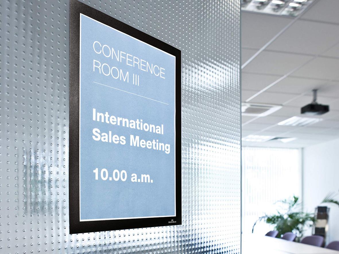 Svart självhäftande Duraframe för A4 med konferensinformation på vägg i kontorsmiljö