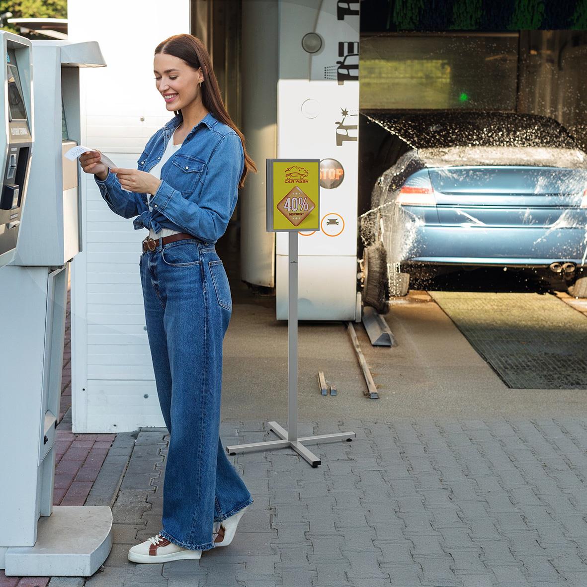 Kvinna använder en utomhus informationsskylt i antracitgrå färg vid en automat