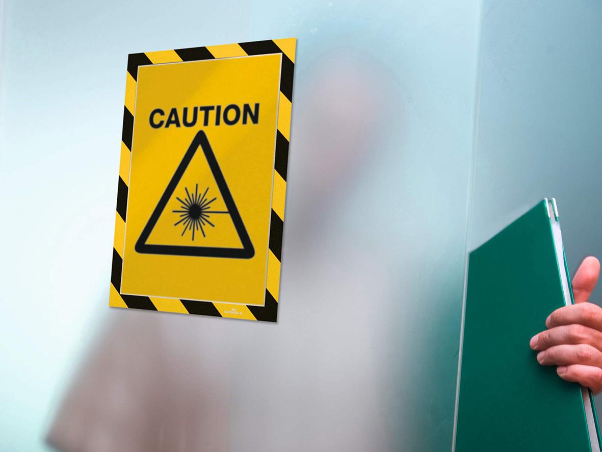 Gul och svart självhäftande säkerhetsvarningsskylt med text CAUTION och laserstråle symbol