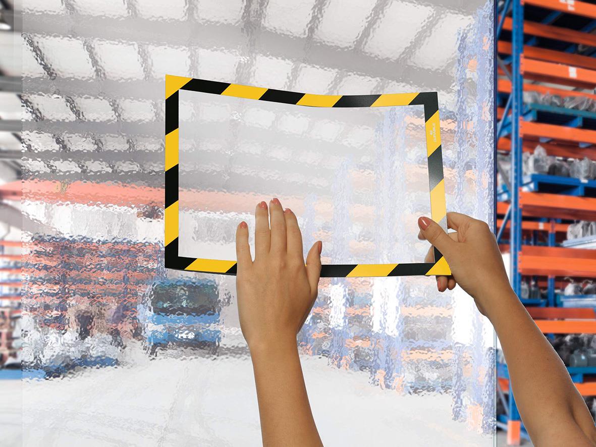 Person monterar Duraframe självhäftande säkerhetsram i gul/svart på glas