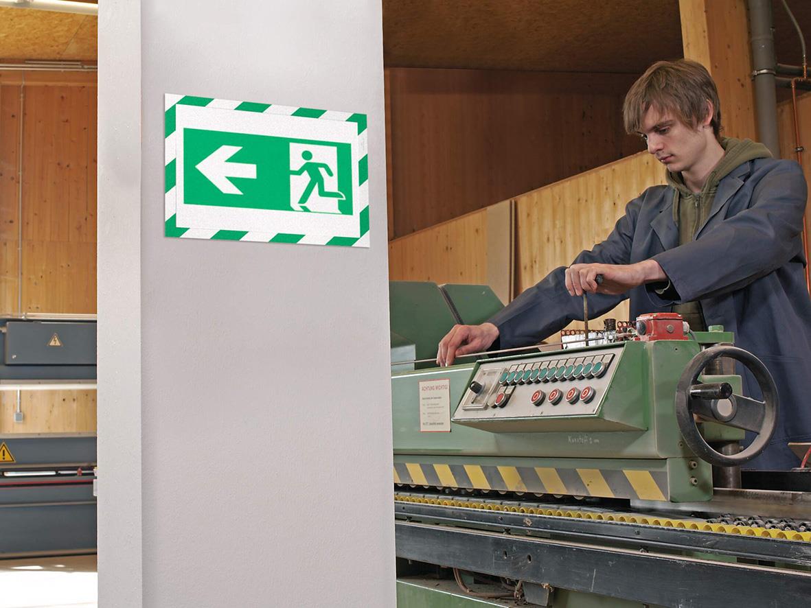 Person som arbetar med maskin i verkstad, säkerhetsutgångsskylt på vägg