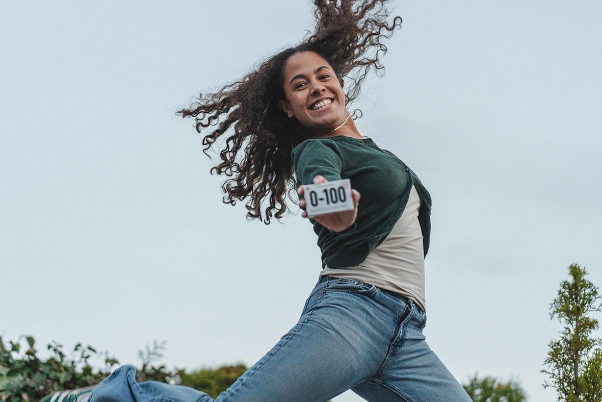 Ung kvinna leker med en telefon som visar 0-100, utomhus mot en blå himmel