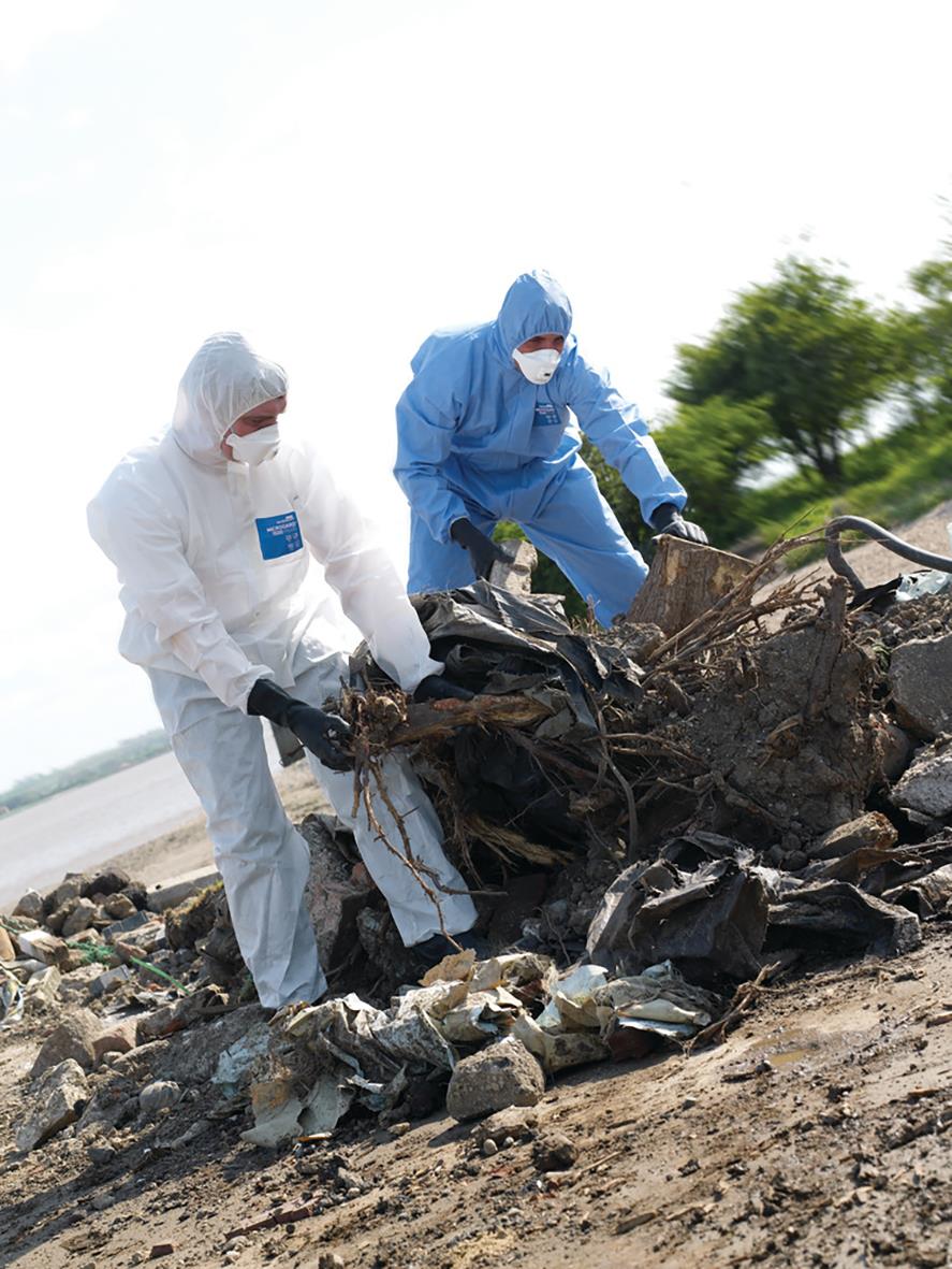Två personer i skyddskläder samlar skräp på en strand
