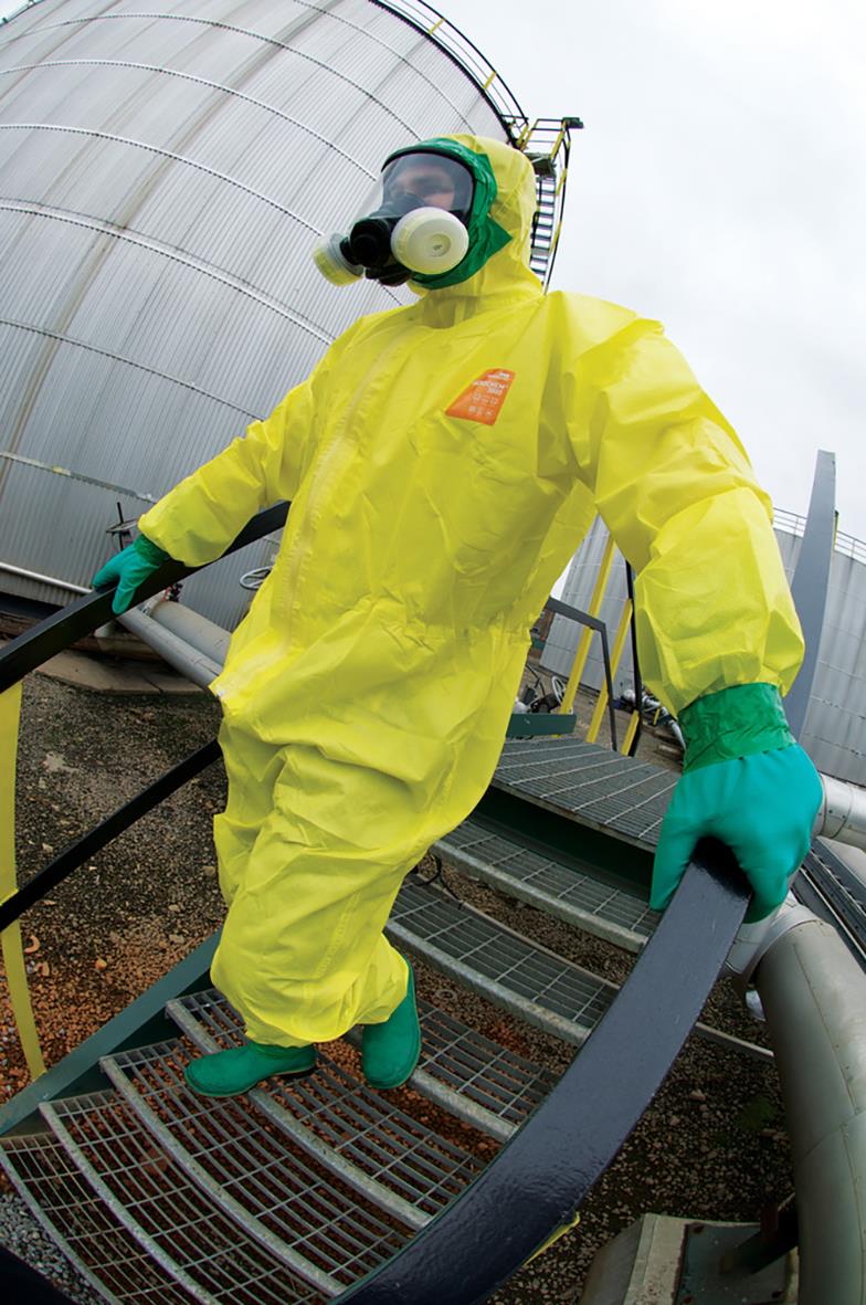 Person i gul korttidsoverall AlphaTec 3000 med skyddsglasögon, andningsskydd och gröna handskar på industriell plats