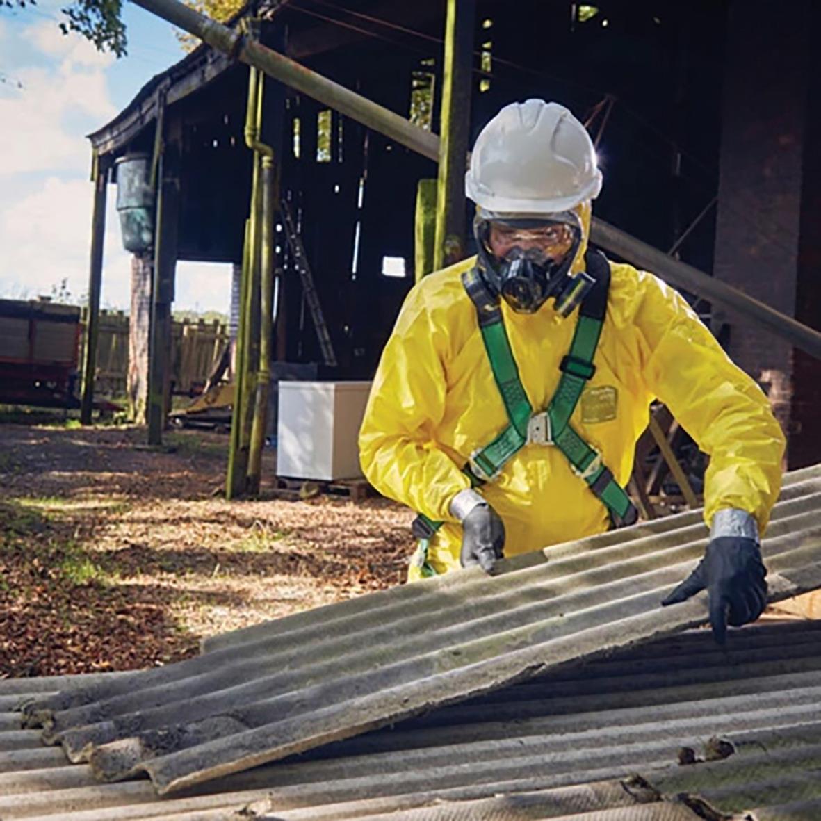 Person i gul korttidsoverall och skyddsutrustning arbetar med takmaterial utomhus