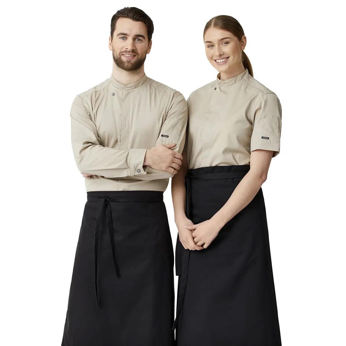 Två personer i beige kock-/servicejackor och svarta förkläden, står sida vid sida och ler