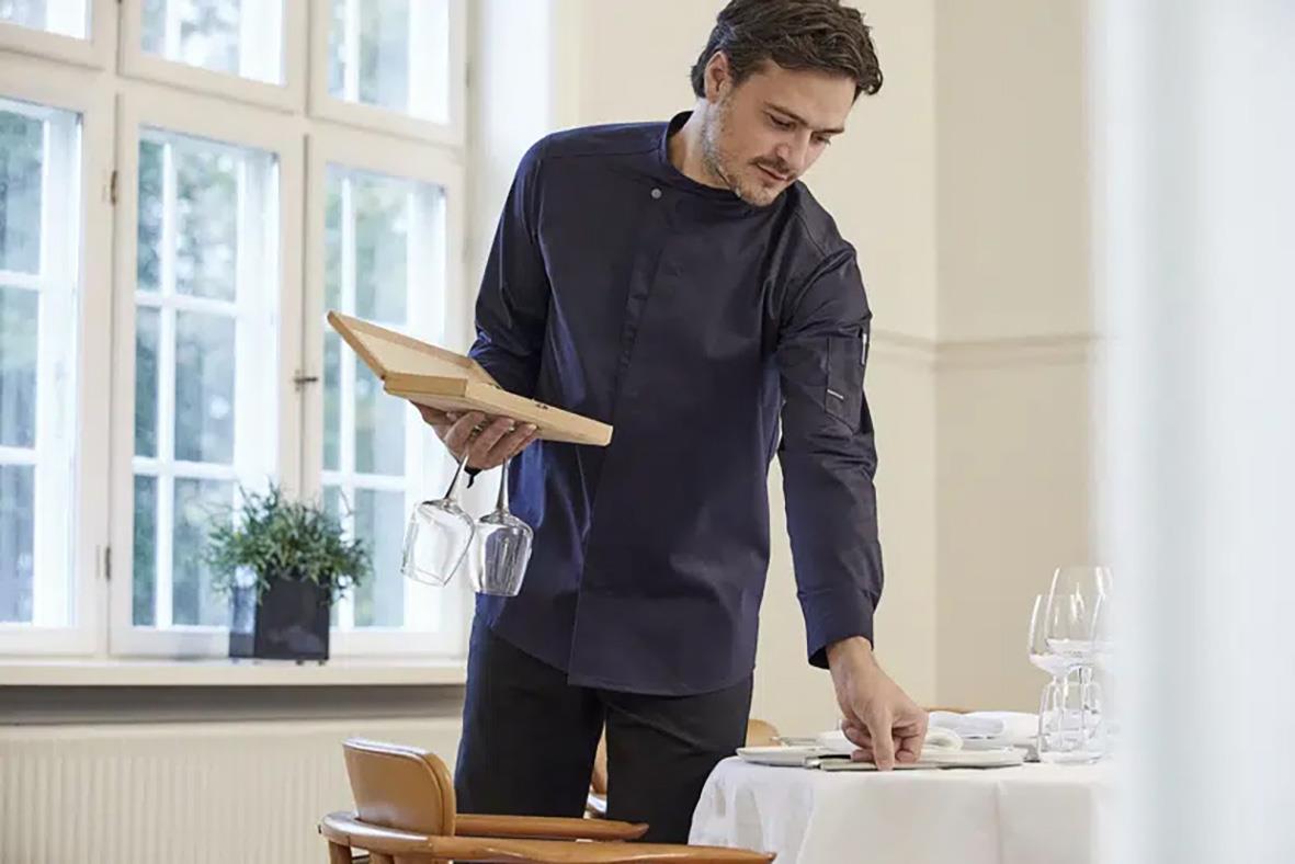 Man i mörk marin kock-/servicejacka som dukar ett bord i ett kök