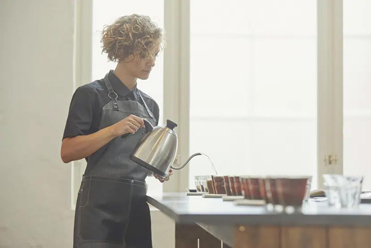 Person som häller vatten från en kanna i ett kök eller serveringsutrymme