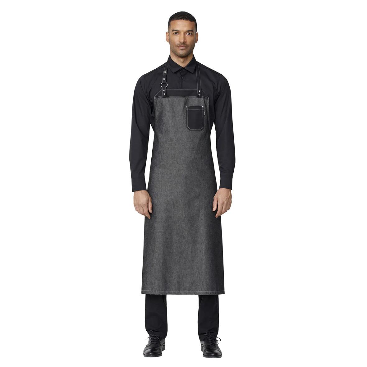 Man bär ett svart bröstlappsförkläde i grått tyg, knäppt över en svart skjorta och byxor, står mot vit bakgrund