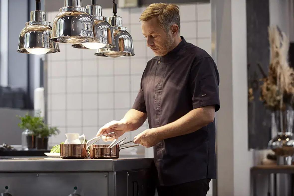 Kock i mörk marin servicejacka Kentaur 23516 står vid köksbänk och lagar mat