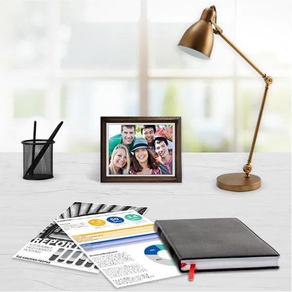 Skrivbord med svart fotoalbum, dokument, pennor, guldfärgad skrivbordslampa och ett foto av ett glatt gäng