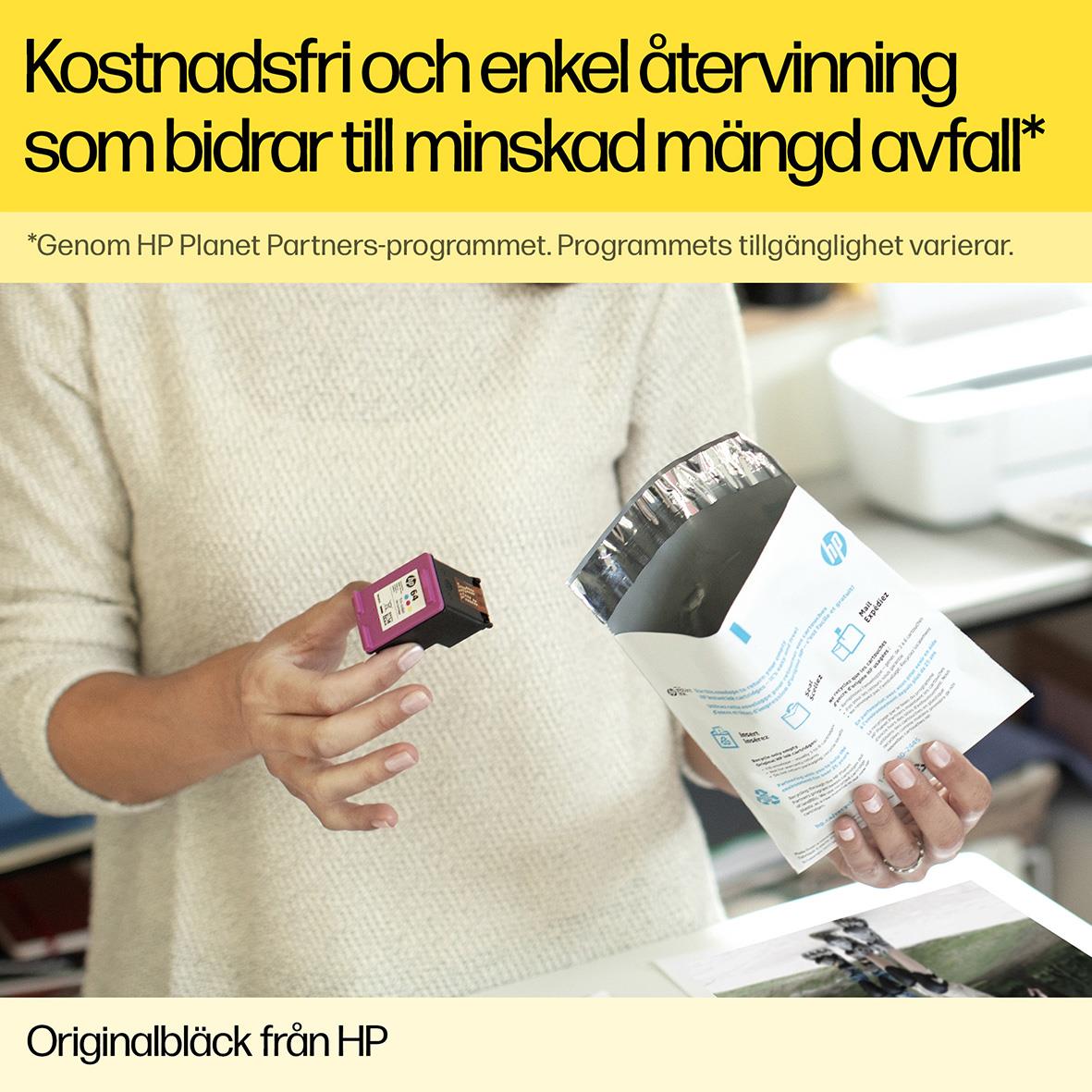 Person håller i en svart HP bläckpatron nr 907 XL och ett utskrivet papper, bakgrund med skrivare och skrivbord