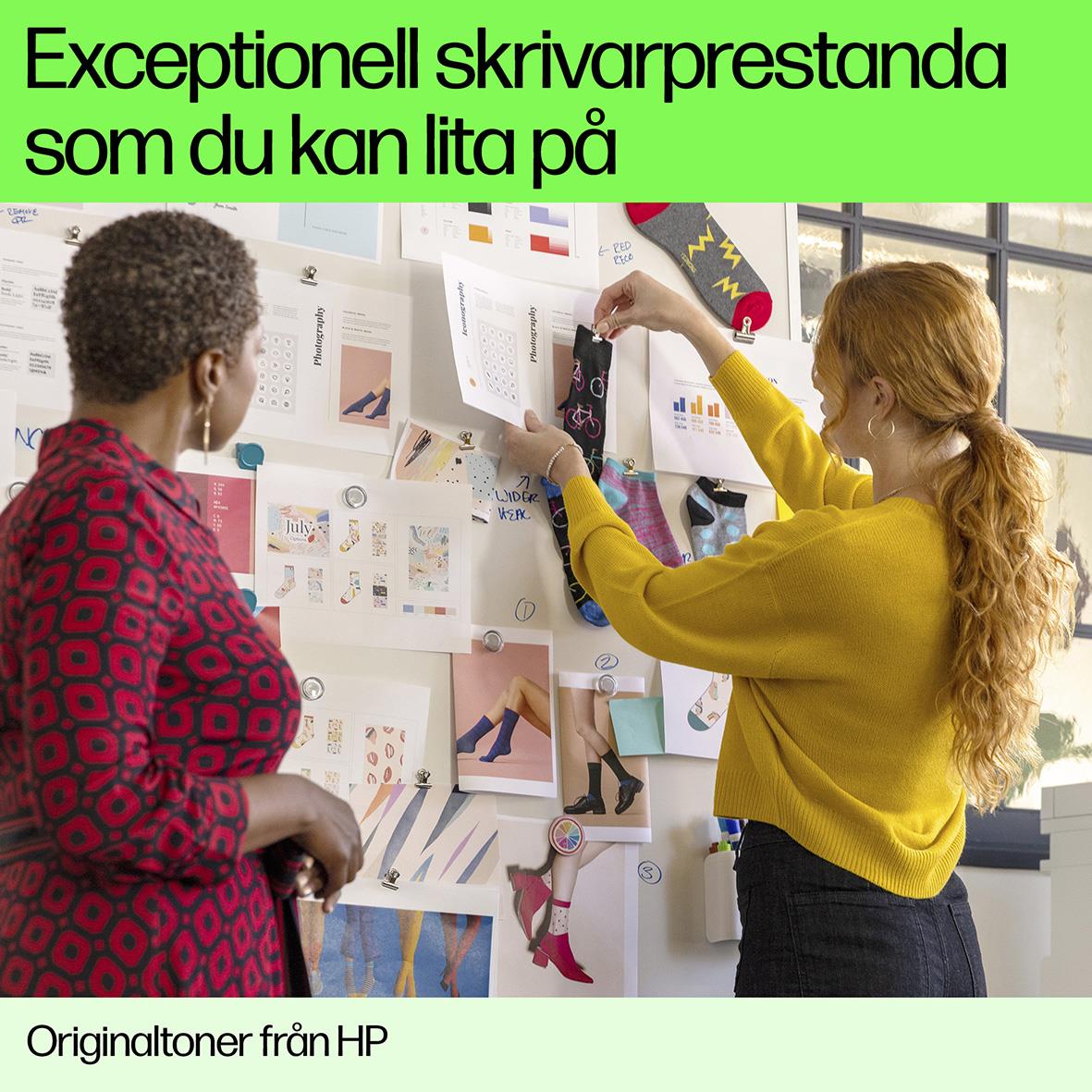 Två kvinnor tittar på utskriftsmaterial på en vägg, en håller en gul laserpatron från HP