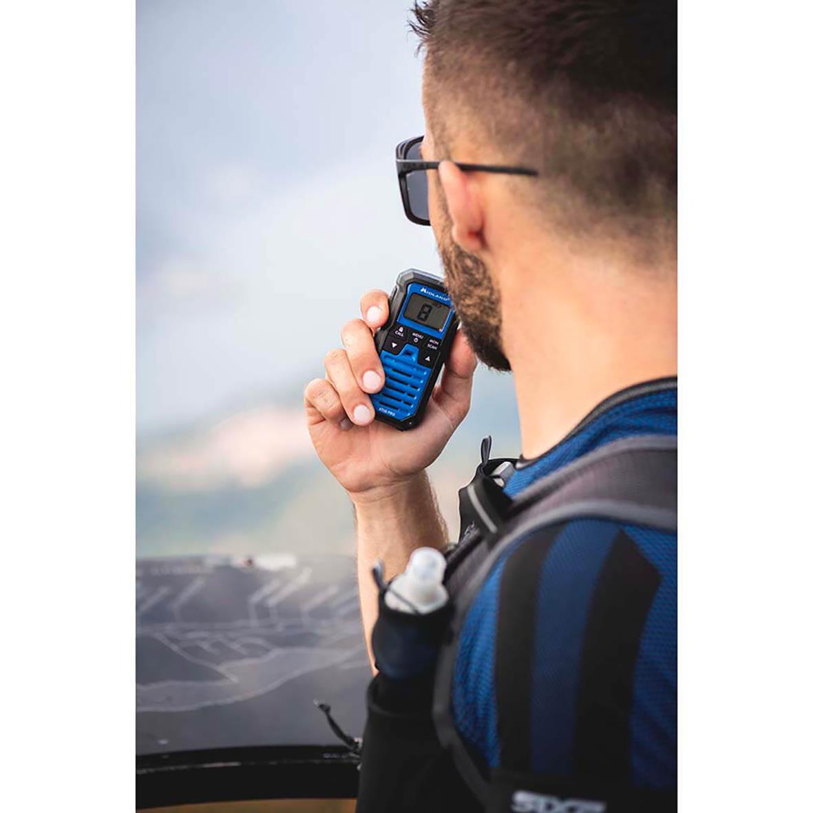 Man med glasögon och backpack använder Walkie Talkie Midland XT50 Pro Duo svart/blå