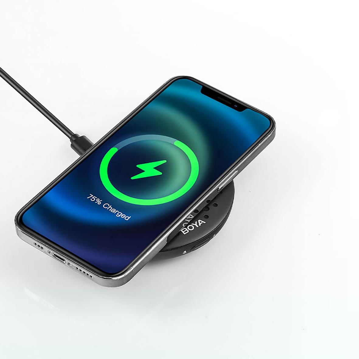 Smartphone laddas trådlöst på en svart laddningsplatta med en mikrofon i bakgrunden