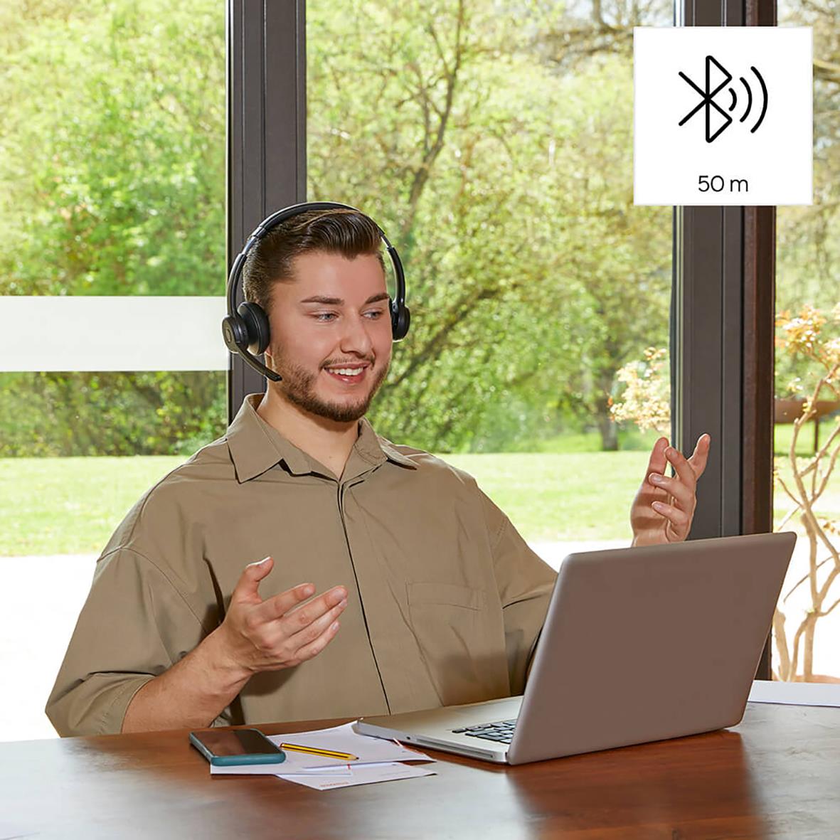 Ung man med headset och laptop i ett rum med stora fönster och grön utomhusbakgrund