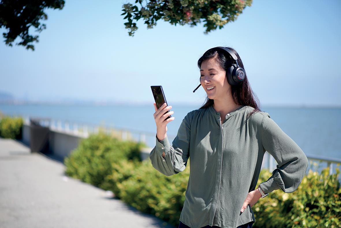 Kvinna med Bluetooth-headset H300 utomhus vid vattnet, tittar på mobil och ler