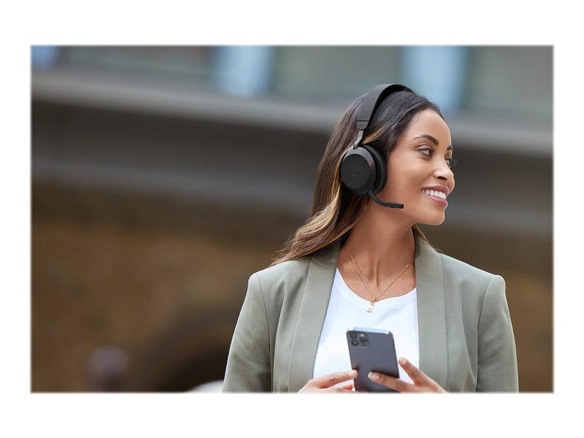 Kvinna med Jabra Evolve2 75 Bluetooth brusreducerande headset utomhus, håller en smartphone och ler