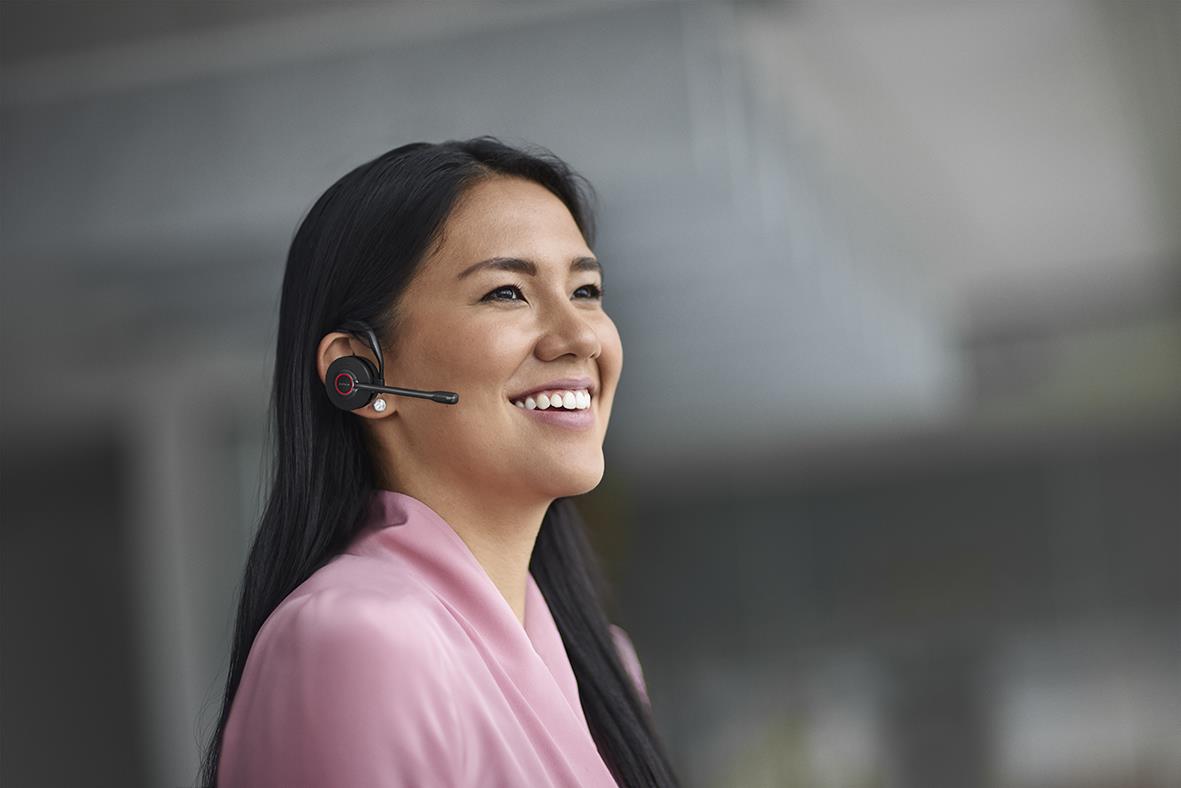 Kvinna med svart headset Jabra Engage 45 SE Stereo, ler och arbetar i ett kontorsmiljö