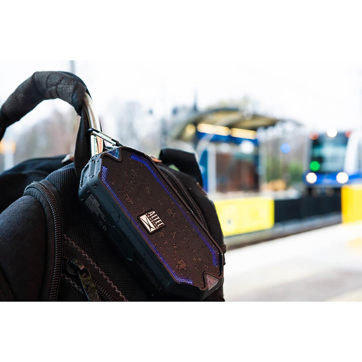 Högtalare Altec Lansing IMV1000 HydraMini RGB IPX67 hålls av en person med handskar, med en stadsmiljö i bakgrunden