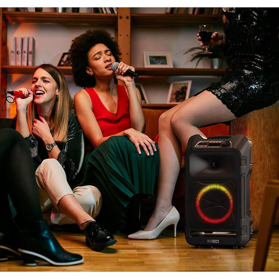 Tre kvinnor som sjunger och dansar med en svart högtalare Altec Lansing IMT9000 SonicBoom100 i ett vardagsrum