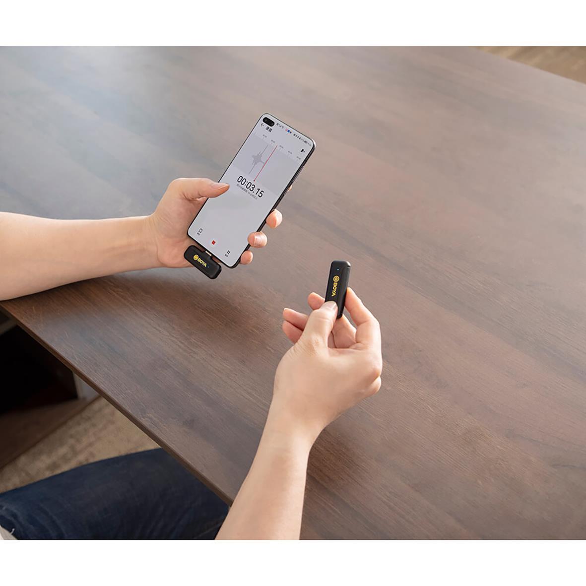 Person håller ett trådlöst mikrofonmottagare och en smartphone med en timer på skärmen på ett träbord