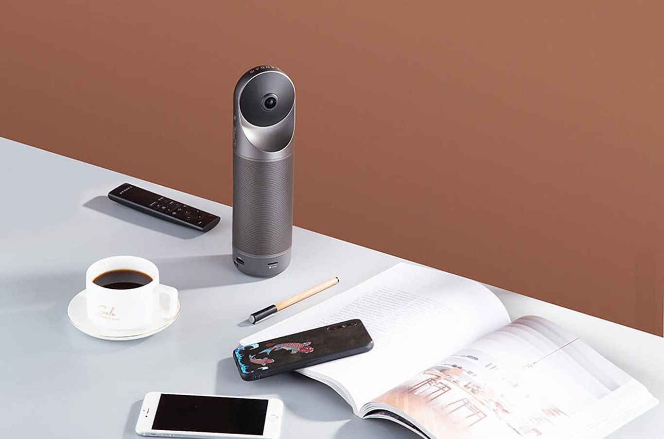 Konferenskamera Kandao Meeting Pro på skrivbord med kaffekopp, fjärrkontroll, mobil och anteckningsblock