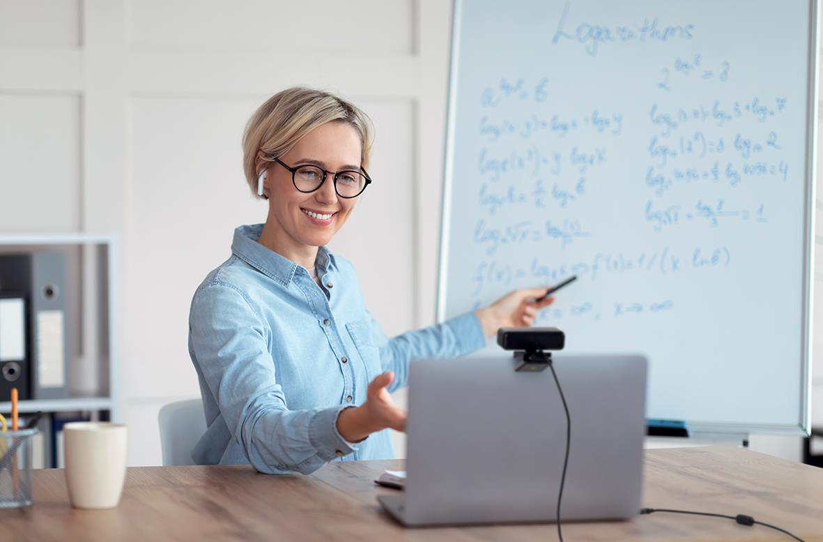 Kvinna i kontorsmiljö använder webbkamera för videokonferens framför vit tavla med skrivning