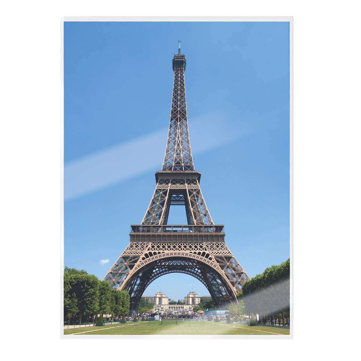 Eiffeltornet sett från marken med blå himmel och gröna träd i förgrunden