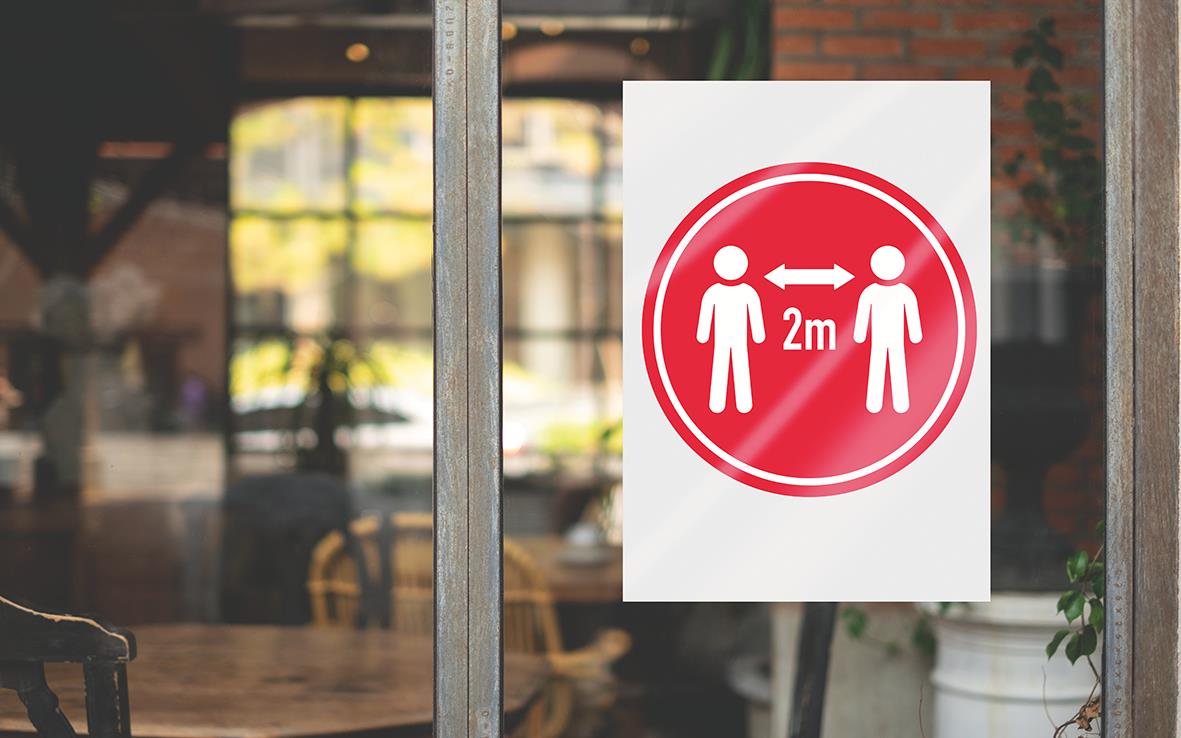 Informationsskylt om 2 meters avstånd mellan personer, placerad på glasruta