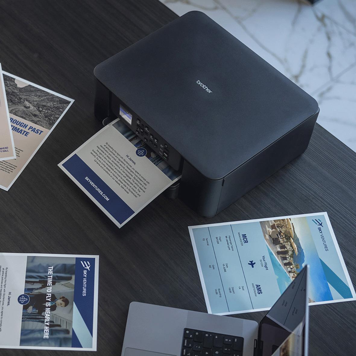 Multifunktionsskrivare Brother DCP-J1310DW på skrivbord med utskrivna dokument och en laptop