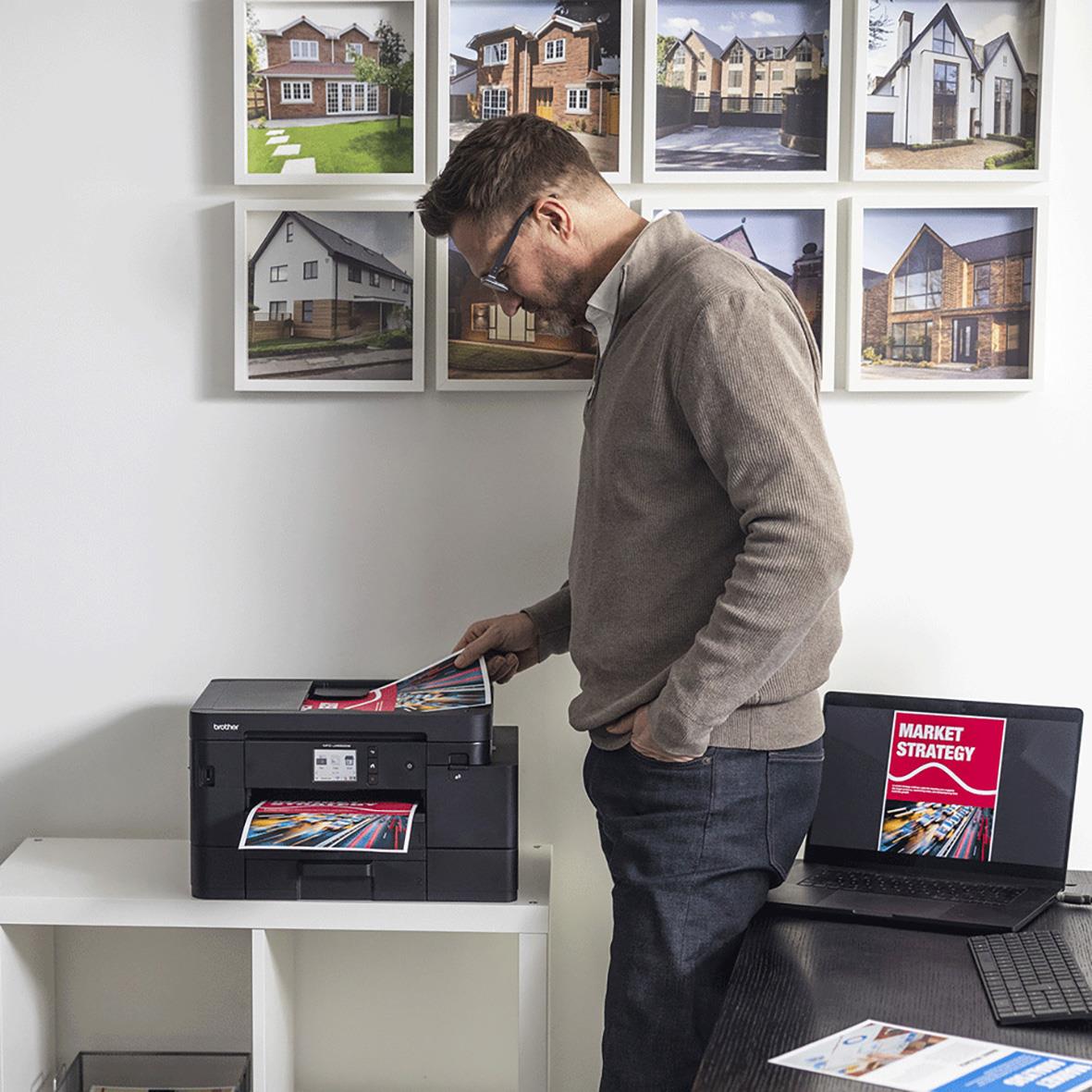 Man använder multifunktionsskrivare Brother MFC-J4550DW i ett kontor med bilder på hus på väggen