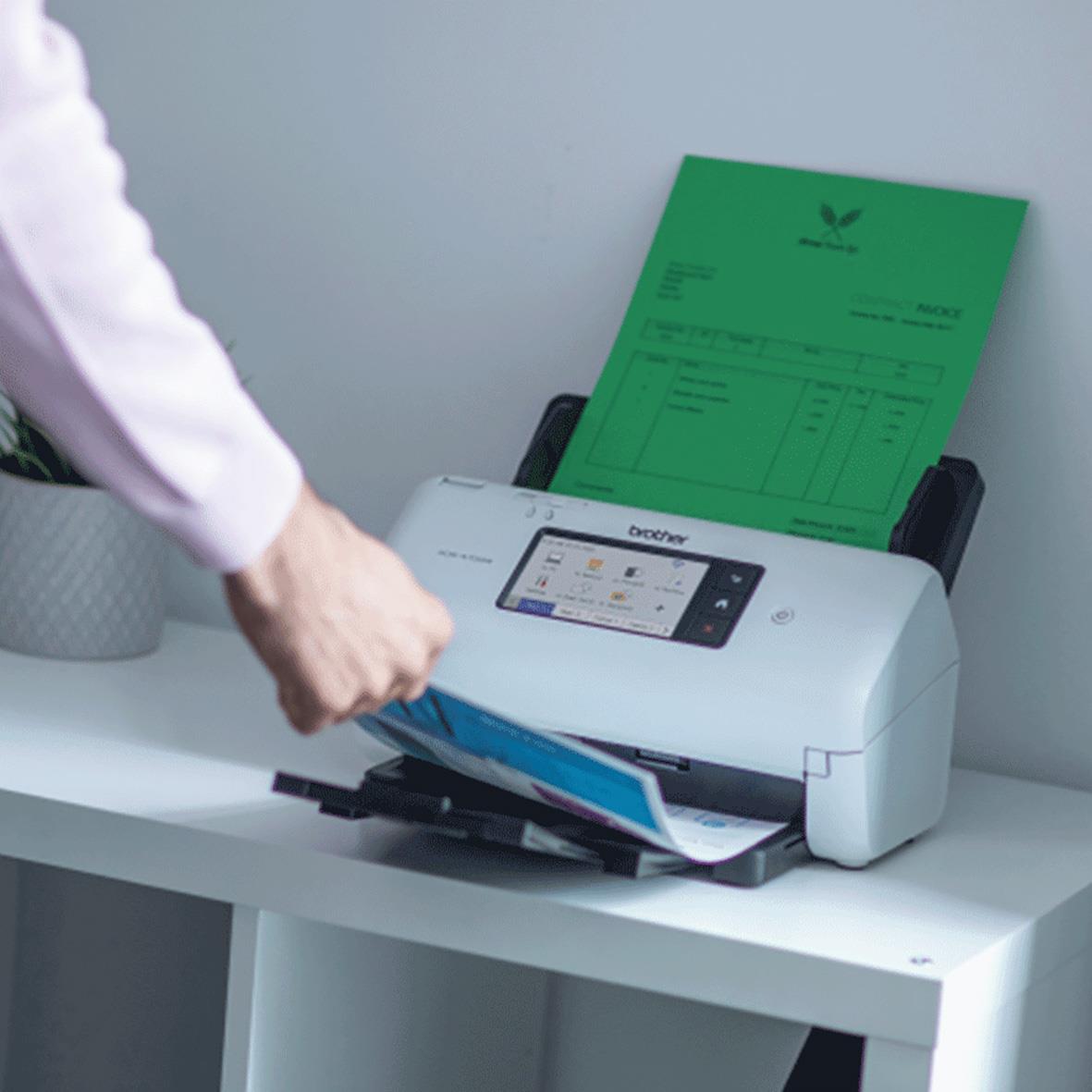 Person använder Brother ADS-4700W skanner för att digitalisera dokument på ett skrivbord
