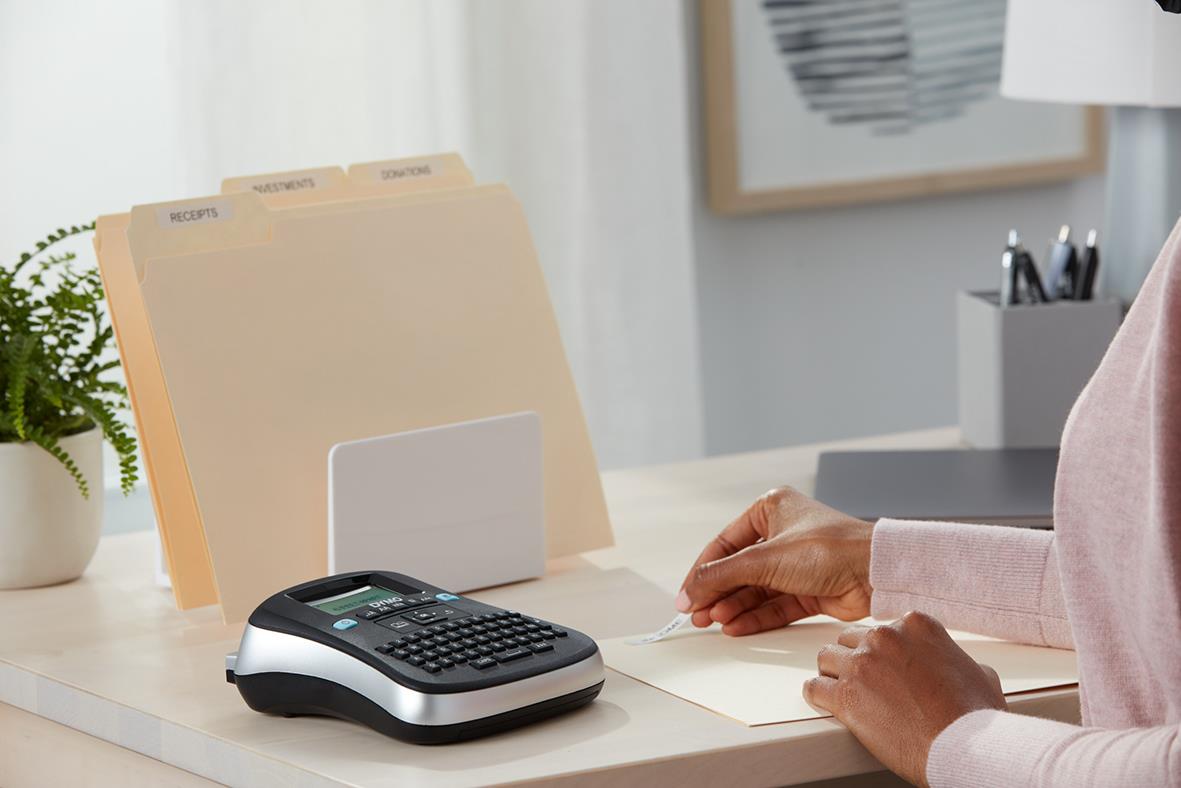 Person skriver på papper bredvid Dymo LabelManager 210D märkmaskin på skrivbord