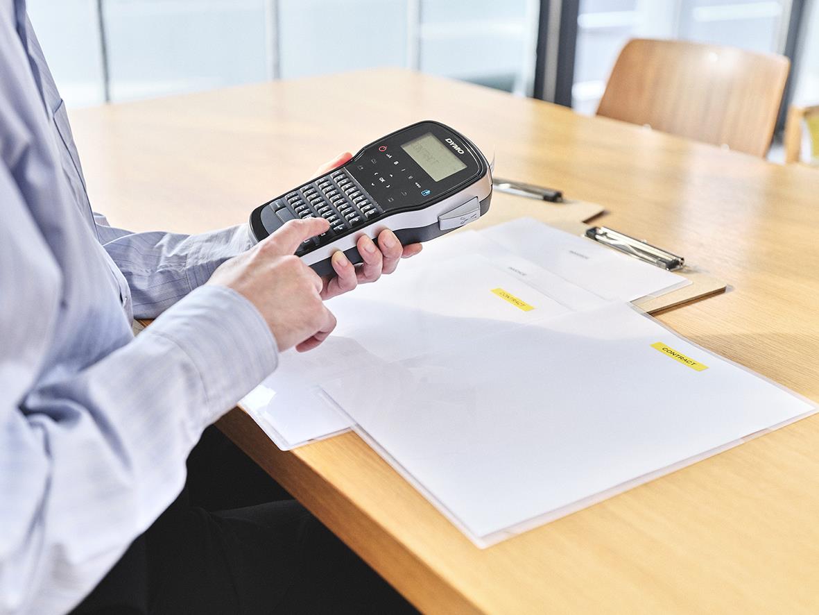 Person håller i en Dymo LabelManager 280 märkmaskin på ett bord med papper och penna