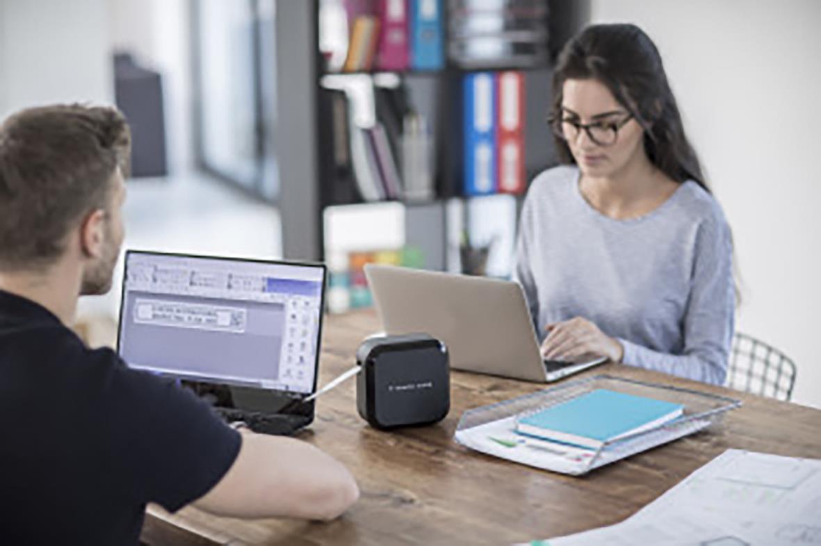 Två personer i ett mötesrum med laptops och märkmaskin Brother P-touch PT-P710BT på bordet