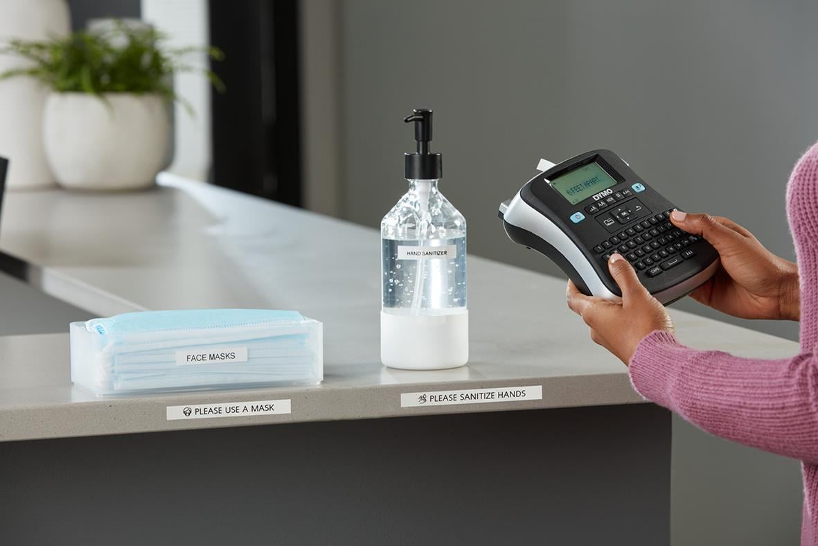 Märkmaskin Dymo LabelManager 210D väskkit med hand som använder en skrivare på ett bord