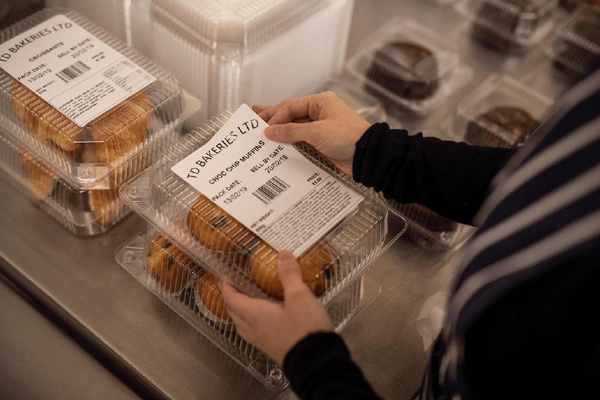 Person som håller i en etikett Brother Papper Vit 102x152mm i en plastlåda i en butik