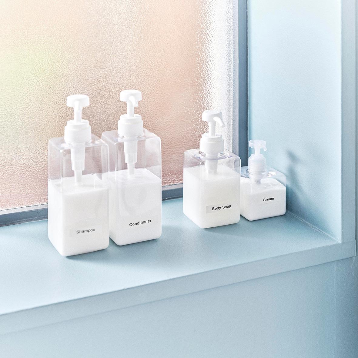Fyra vita pumpflaskor med handtvätt och handkräm på fönsterbräda