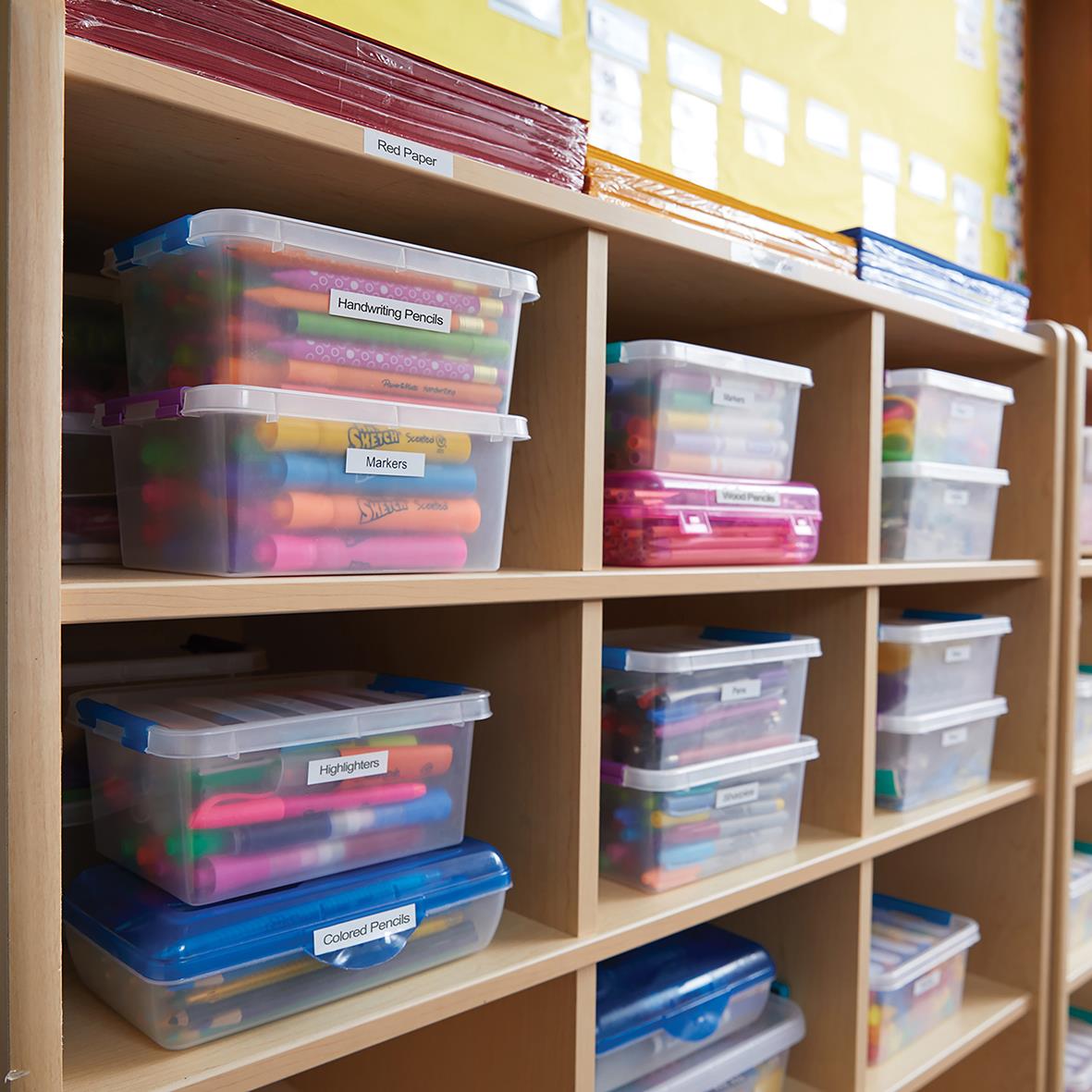 Flera plastlådor fyllda med färgglada märkpennor och etiketter på en trähylla