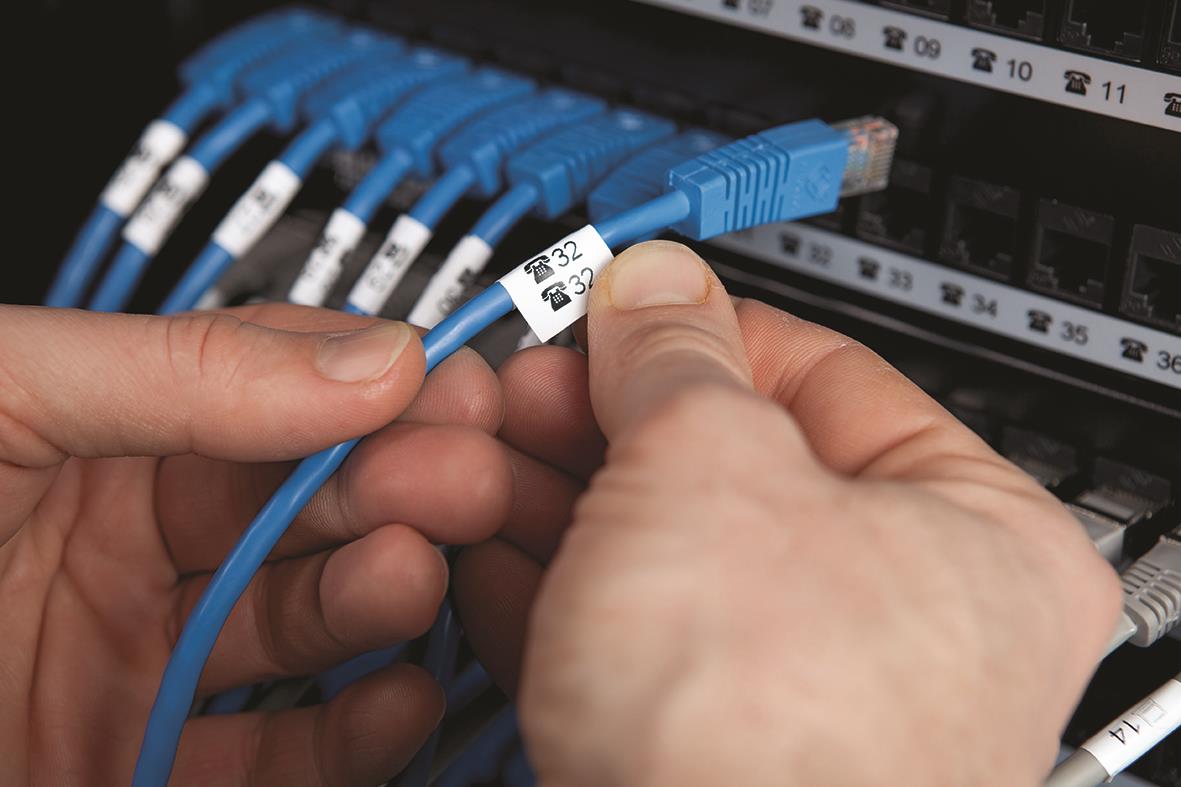 Person som fäster ett svart/gult märkbandsetikett på en nätverkskabel i ett serverskåp