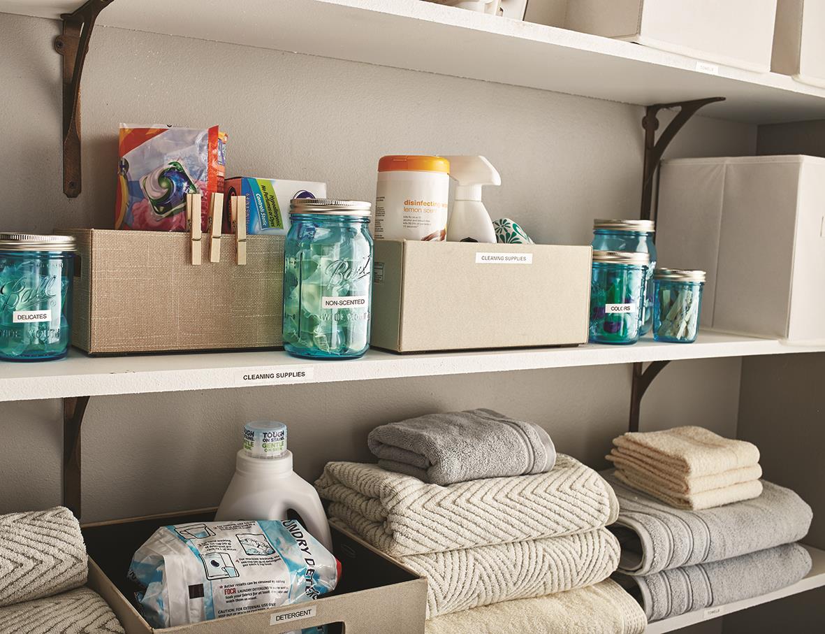 Förvaringshylla med olika burkar, tvättmedel och handdukar i ett skåp