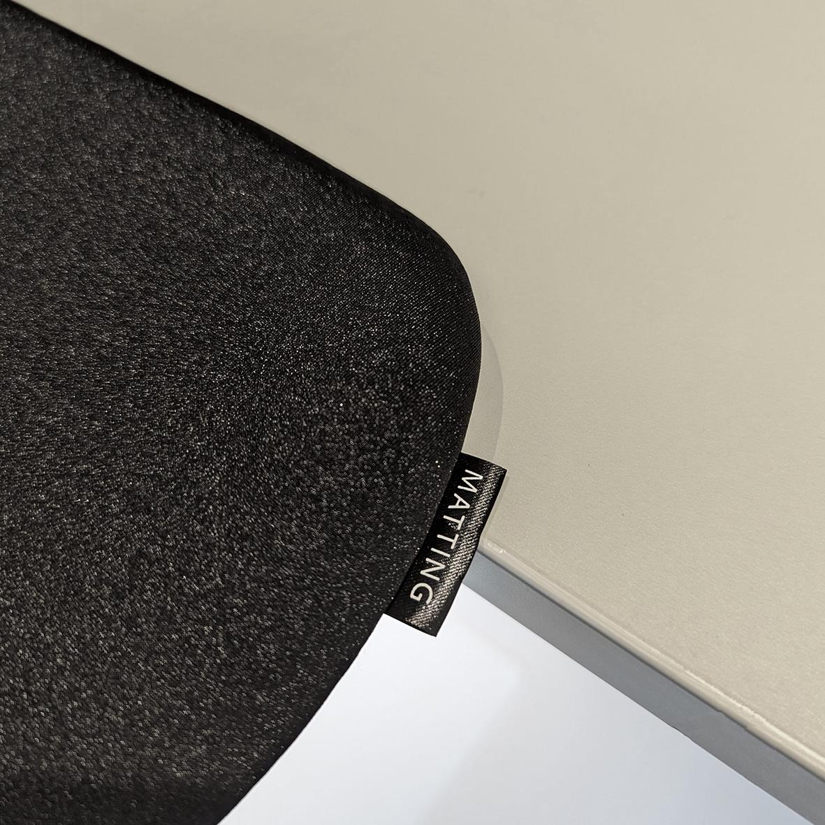 Svart matta med en liten etikett som säger MATTING, placerad på ett golv nära en vägg