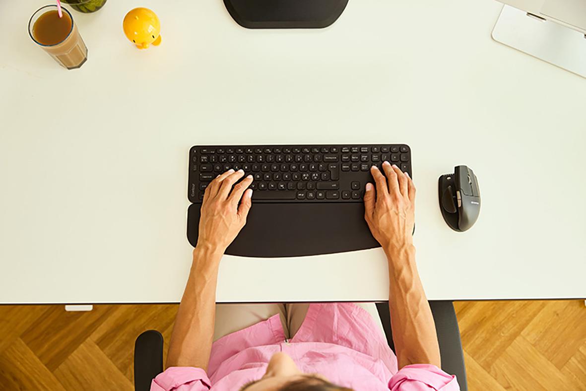 Person som skriver på ett tangentbord vid ett skrivbord med dator och mus