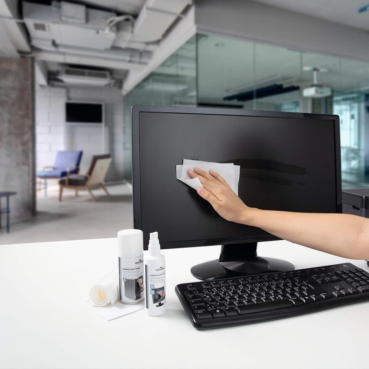 Person rengör en datorskärm med en mikrofiberduk i ett modernt kontorsutrymme