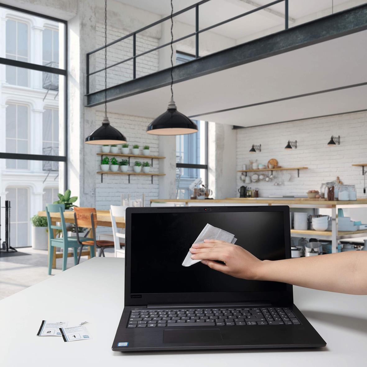 Person som rengör en laptop-skärm med en våt- eller torrduk i ett modernt kök eller kontorsutrymme