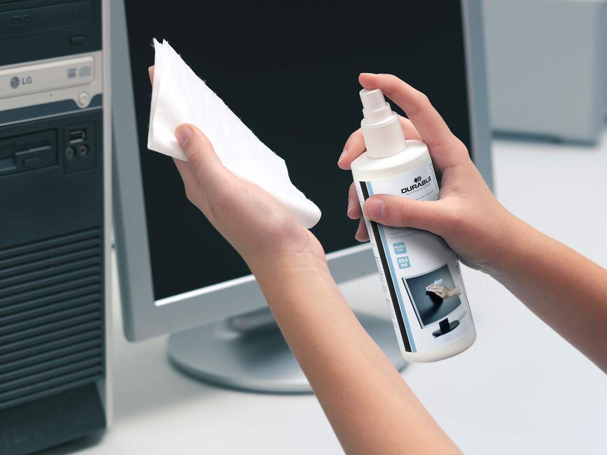Person rengör en datorskärm med spray och mikrofiberduk